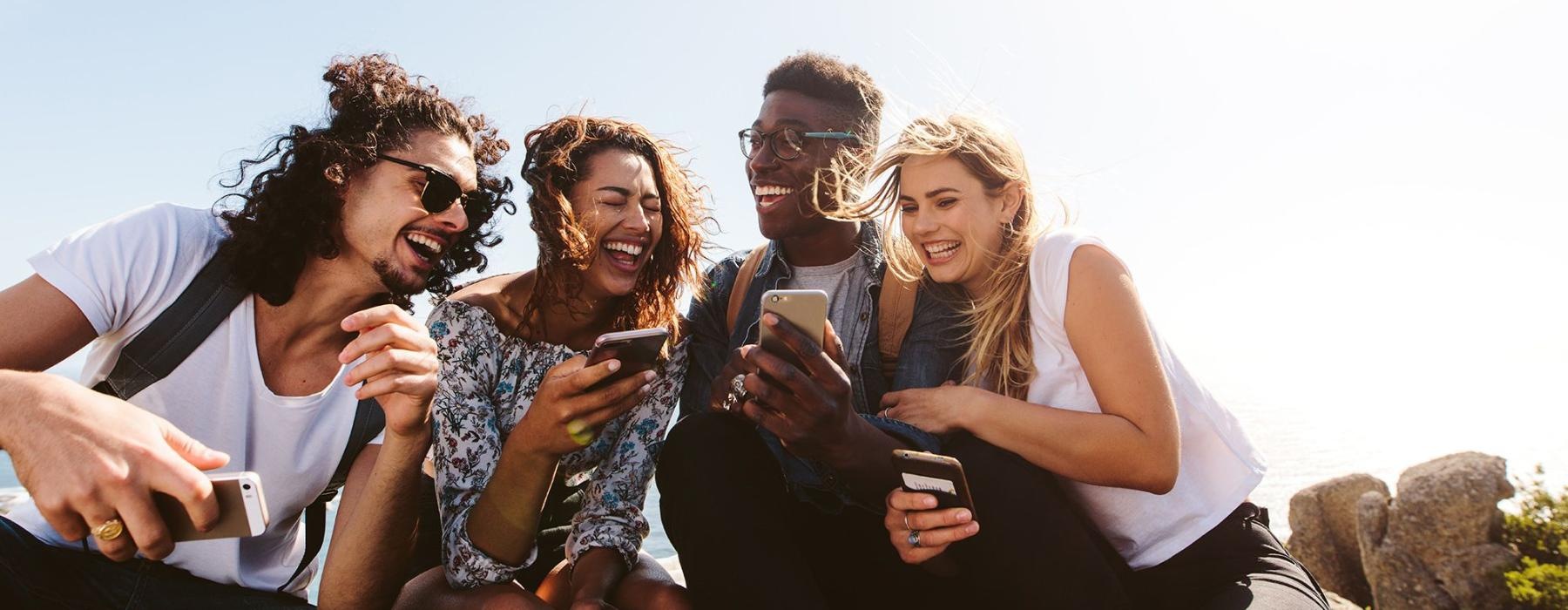 a group of friends sit outside laughing over their cell phones