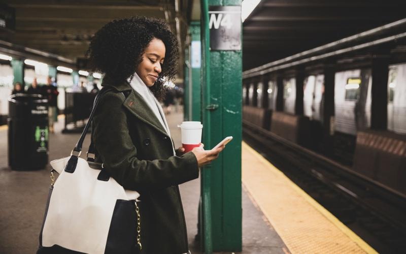 woman with a cup of coffee texts on subway station platform