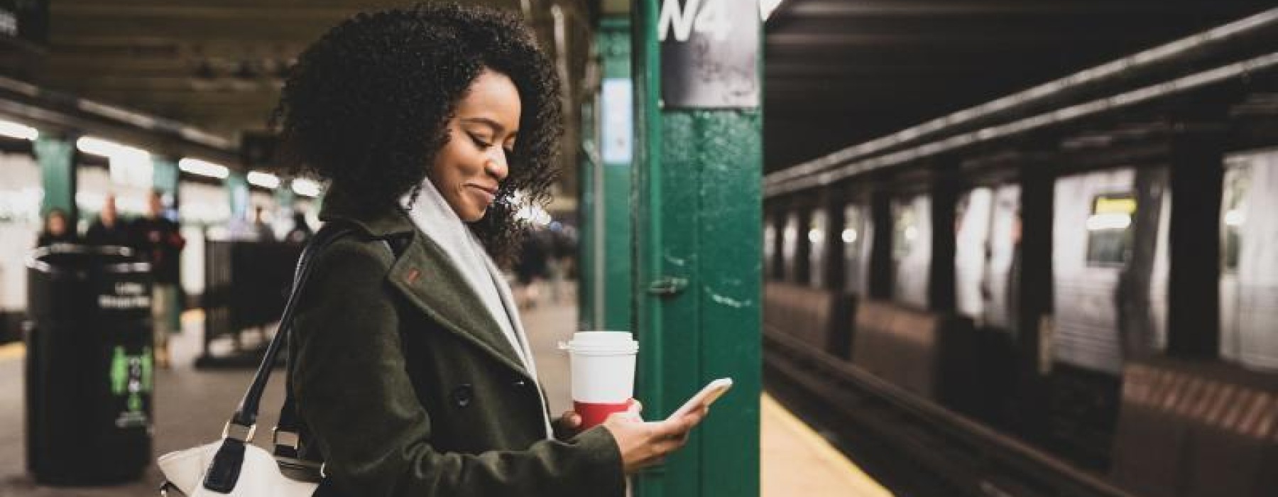 woman with a cup of coffee texts on subway station platform